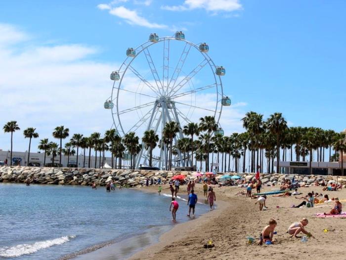 Playa junto al mar con noria, palmeras y ambiente turístico ideal para disfrutar del sol.