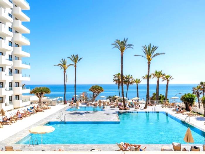 Piscina en primera línea de playa con vistas al mar y palmeras en un ambiente relajante.