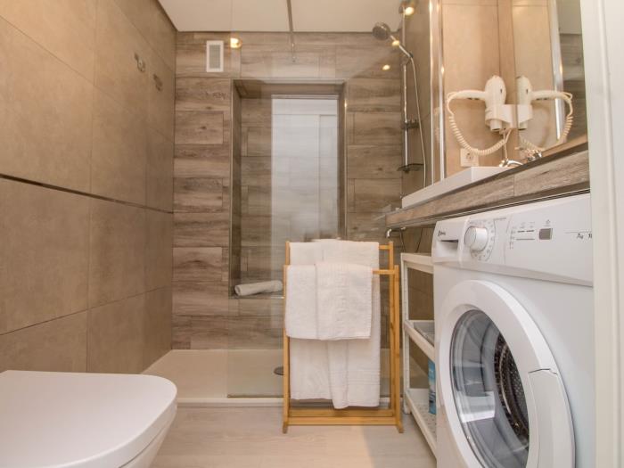 Baño moderno con ducha amplia, lavadora y diseño elegante para una estancia cómoda.