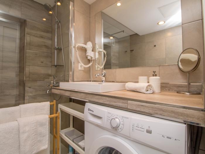 Baño moderno con ducha amplia, lavadora y acabados elegantes para mayor comodidad.