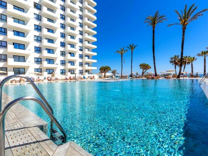 Piscina en primera línea de playa con vistas al mar y palmeras en un ambiente relajante.