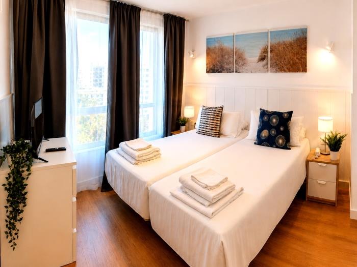 Bright modern bedroom with twin beds, natural light and cozy atmosphere for relaxing stays.