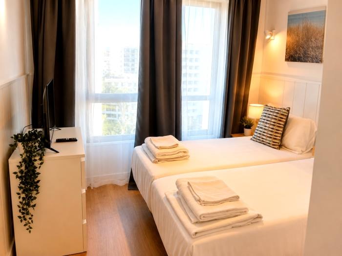 Bright modern bedroom with twin beds, natural light and cozy atmosphere for relaxing stays.